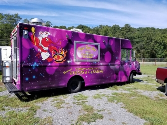 purple wrapped food truck with yellow lettering parked in gravel