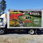 wrapped box truck showing green lawn care and pest control advertisements
